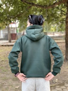 A person standing with their back to the camera, wearing a dark green hoodie and light gray sweatpants. 