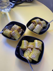 Three small black bowls contain rolled pastries topped with sesame seeds and filled with a brown mixture. 